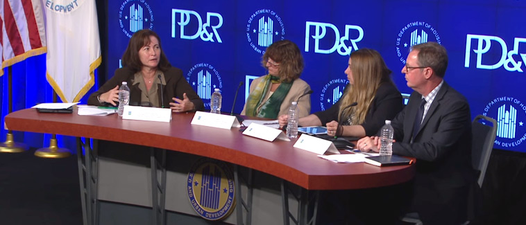 Image showing four individuals, Principal Deputy Assistant Secretary of HUD’s Office of Community Planning and Development Harriet Tregoning and three panelists, seated at a table bearing the HUD logo. An image with the HUD and PD&R logos is visible on a screen behind the table.